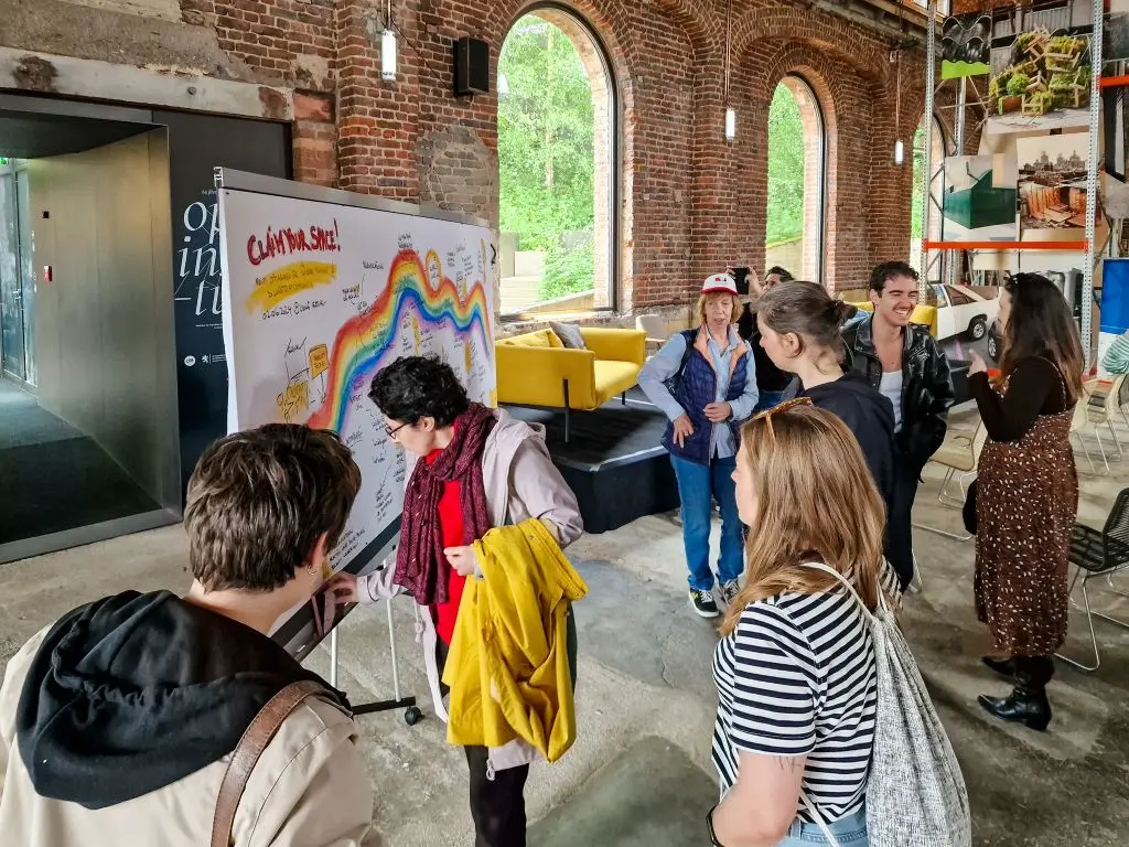 Visitors reading a large graphic recording panel in an industrial brick hall